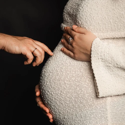 Hands resting on a pregnant belly in a textured cream knit